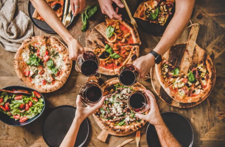 The Best Cheap Food and Drinks in Las Vegas When You’re on a Budget 2 Dining in downtown Las Vegas. An aerial view of a variety of pizzas as friends make a toast with their wine glasses above it.